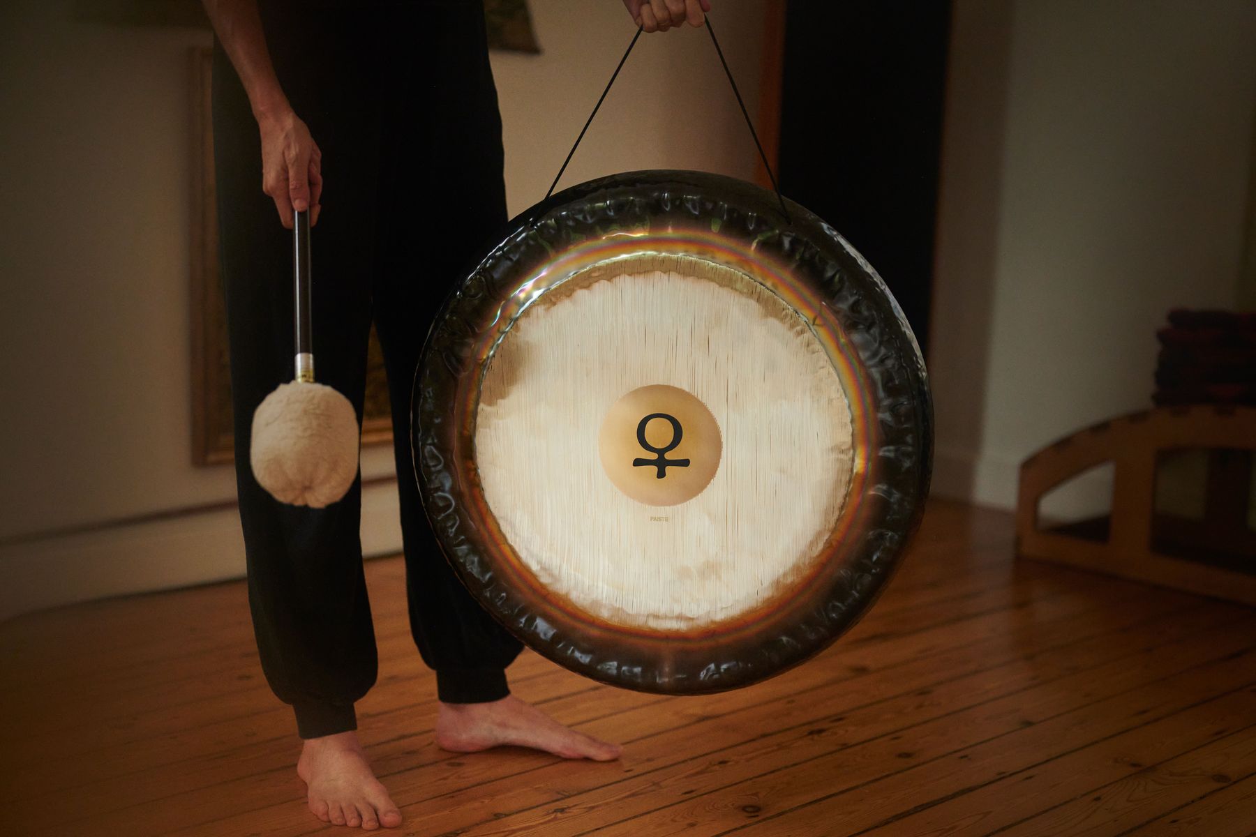 A player holds a Venus planetary gong and a felt mallet on a wooden floor