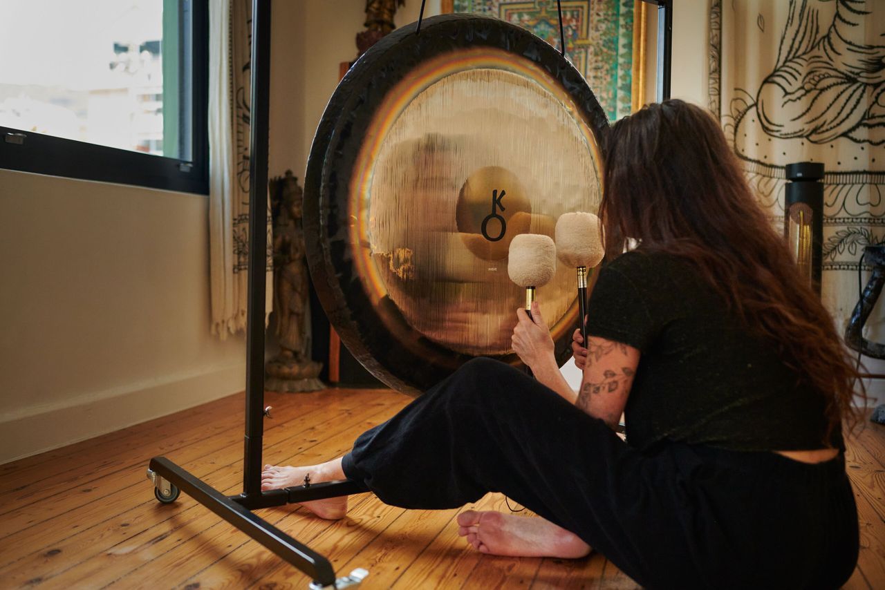 A player sits on the floor beside a planetary gong, mallets in hand