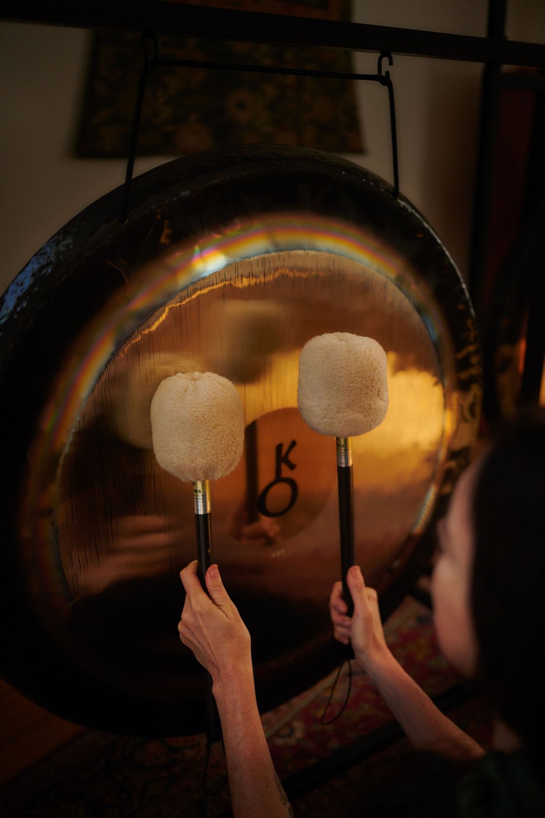 Two mallets rest against a glowing Paiste gong